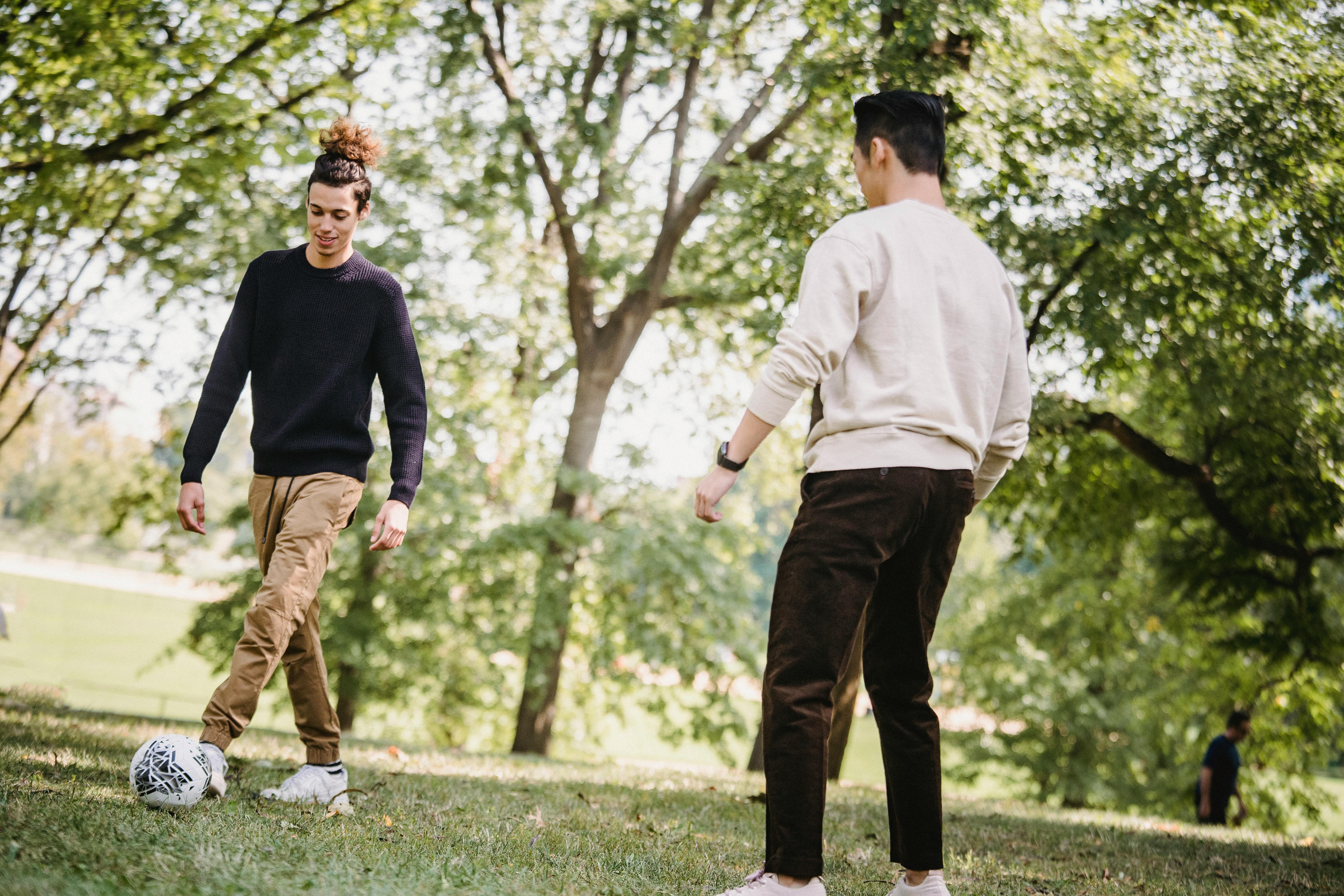 positive ethnic male friends playing football in park