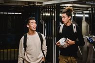 Cheerful ethnic male friends in casual sweaters with backpacks and soccer ball walking in modern metro station and having conversation