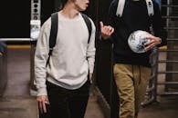 Crop young male friends wearing casual clothes with backpacks and soccer ball walking in modern underground station and chatting