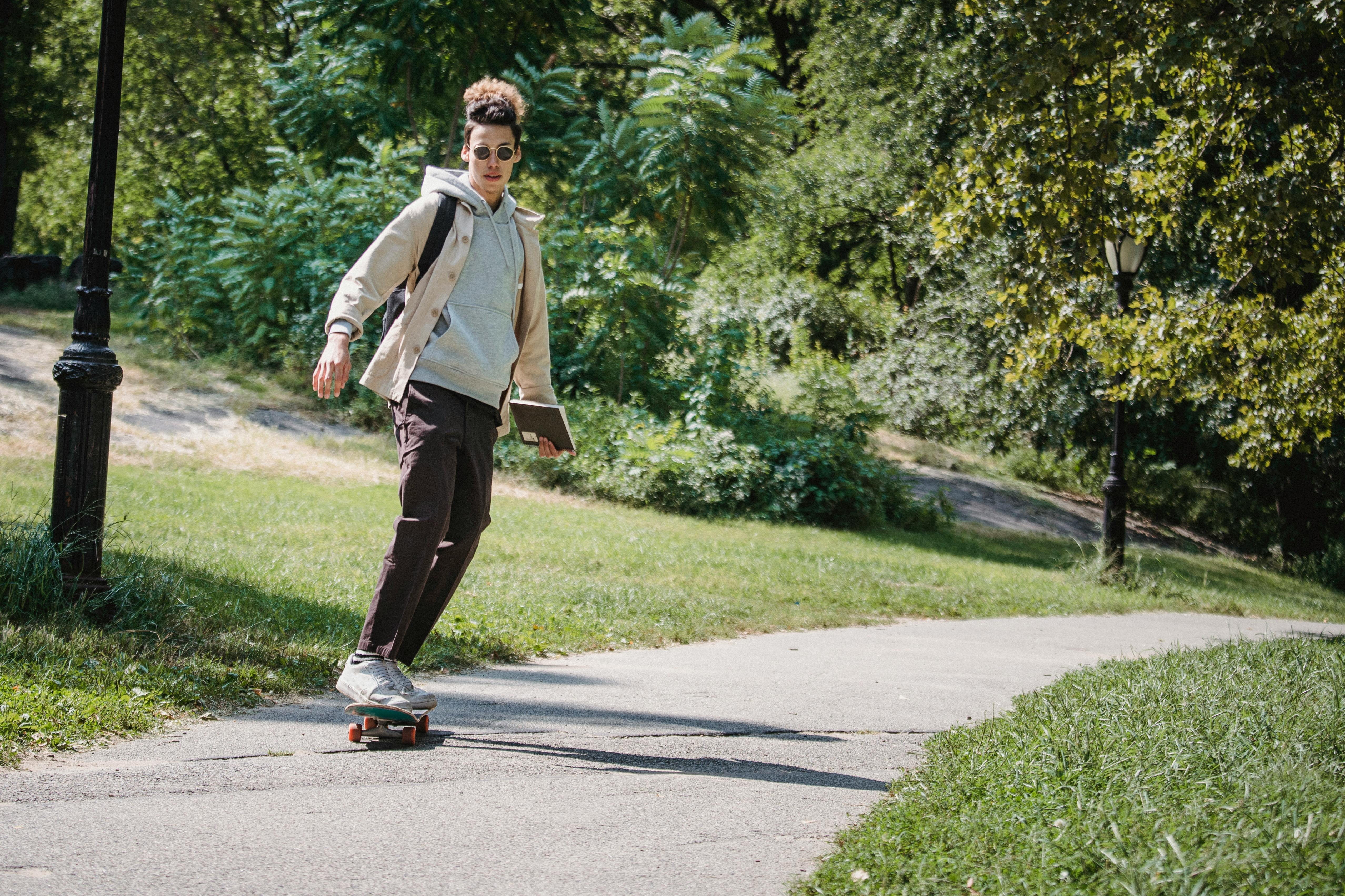 stylish young ethnic guy balancing on skateboard in park