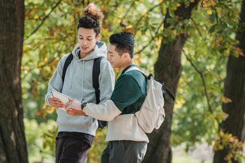 Multiethnic male teenagers reading notebook in park after studies
