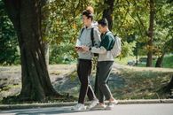 Side view of young stylish diverse male friends in casual outfits and backpacks walking together in path in park and preparing for exam