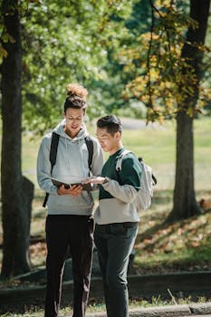 Two young men studying with a tablet in a sunny park, engaged and focused.