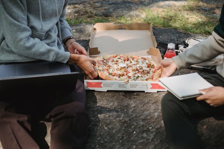 Unrecognizable Male Friends Sitting With Laptop And Pizza On Ground