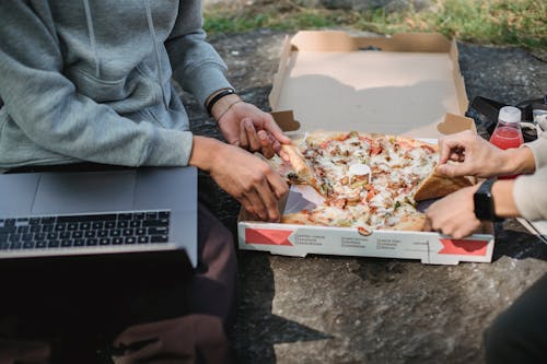 Unrecognizable men sitting outside with computer and pizza