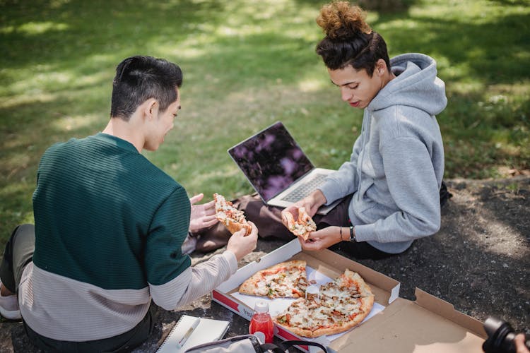 Male Friends Sitting Outside With Computer And Pizza