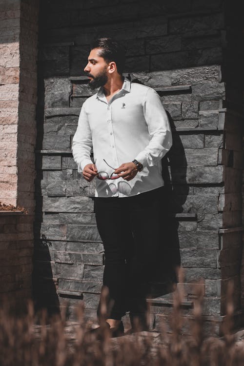 Free Man in White Dress Shirt and Black Pants Standing Beside Brown Brick Wall Stock Photo