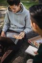 一位男同学在公园吃披萨午餐时，用上网本浏览网页，并在记事本上写作