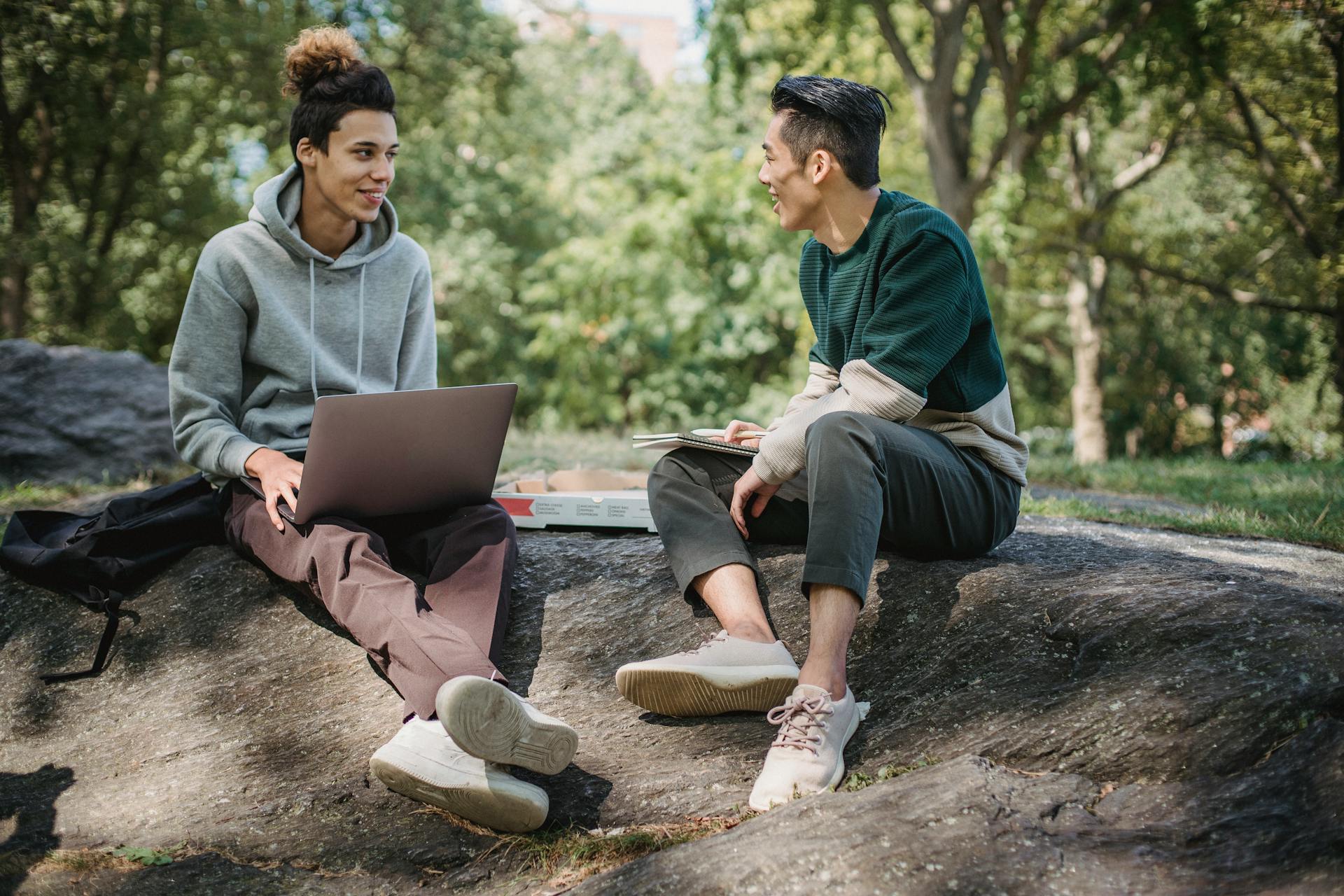 Full body of positive multiracial classmates sharing information on university assignment while browsing laptop in nature