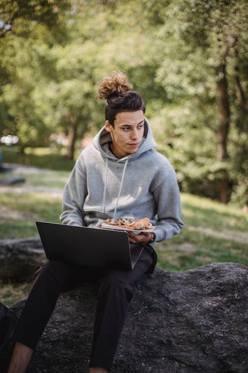 Thoughtful man eating pizza while doing homework on laptop