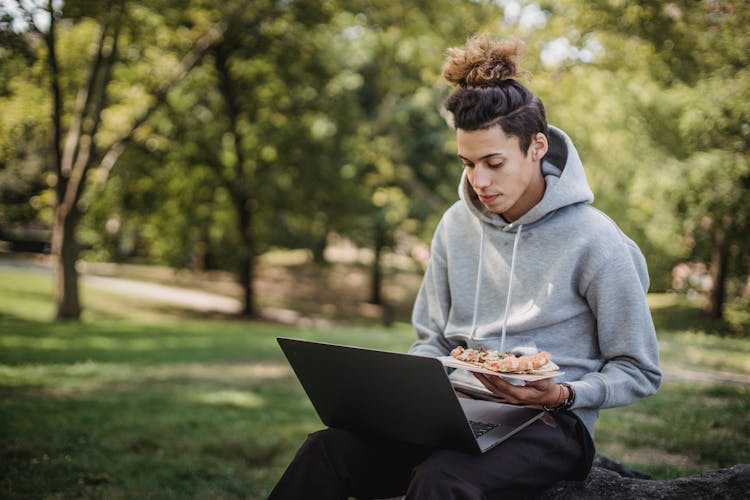 Serious Male Student Using Laptop For Studies At Park