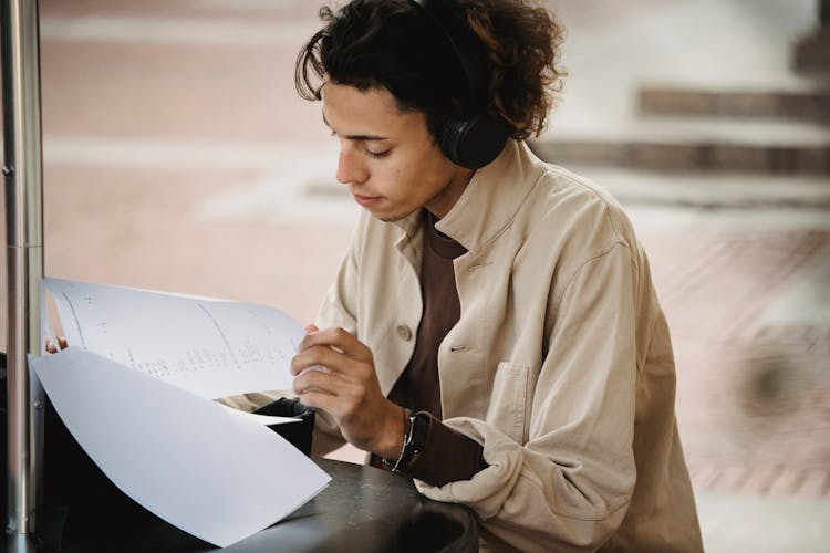 Concentrated Student Reading Documents While Listening To Music In Headphones