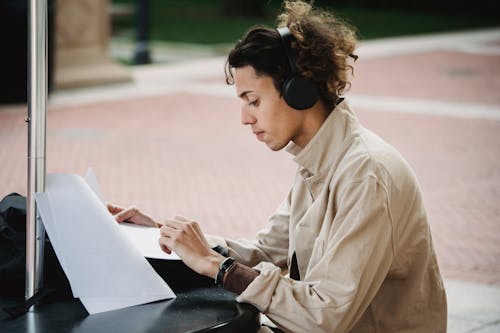 Side view of concentrated male learner preparing report for university assignment while listening to music in wireless headphones