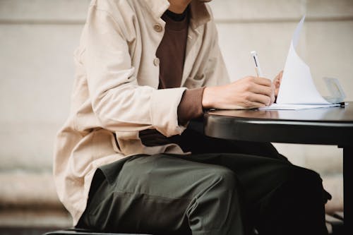 Free Side view of crop anonymous male learner writing in paper documents with pen while doing assignment Stock Photo
