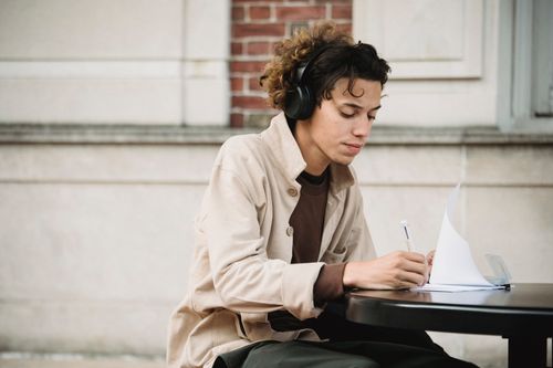 Free Side view of learner writing task in document while preparing university assignment and listening to music in wireless headphones Stock Photo