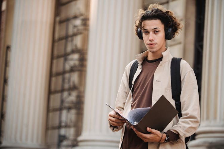 Serious Student In Wireless Headphones With Folder