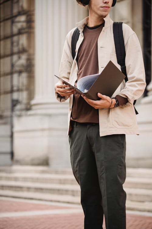 Serious student standing with folder near university building