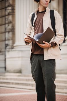 一名年轻人拿着文件夹，专注而随意地站在大学大楼外
