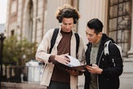 Smiling multiracial classmates turning pages of file on folder with homework task near university