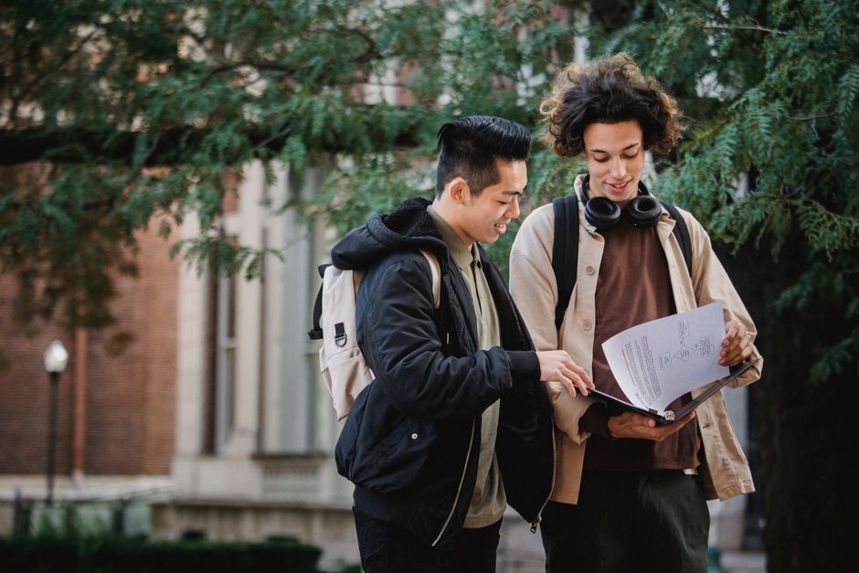 Positive multiracial classmates smiling and turning pages of document in folder while discussing studies together Positive multiracial classmates smiling and turning pages of document in folder while discussing studies together