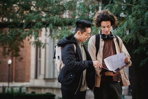 Free Positive multiracial classmates smiling and turning pages of document in folder while discussing studies together Stock Photo