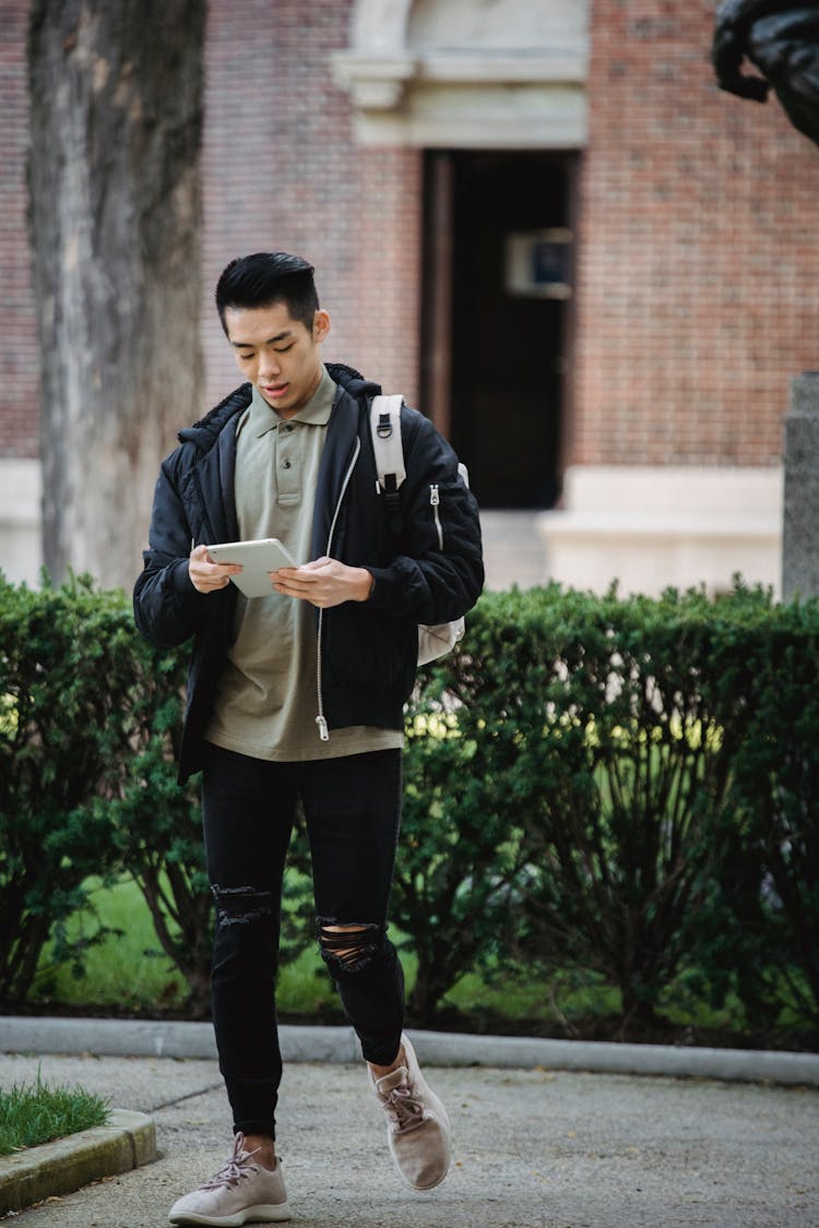 Ethnic Man Using Tablet While Walking On Footpath In Campus