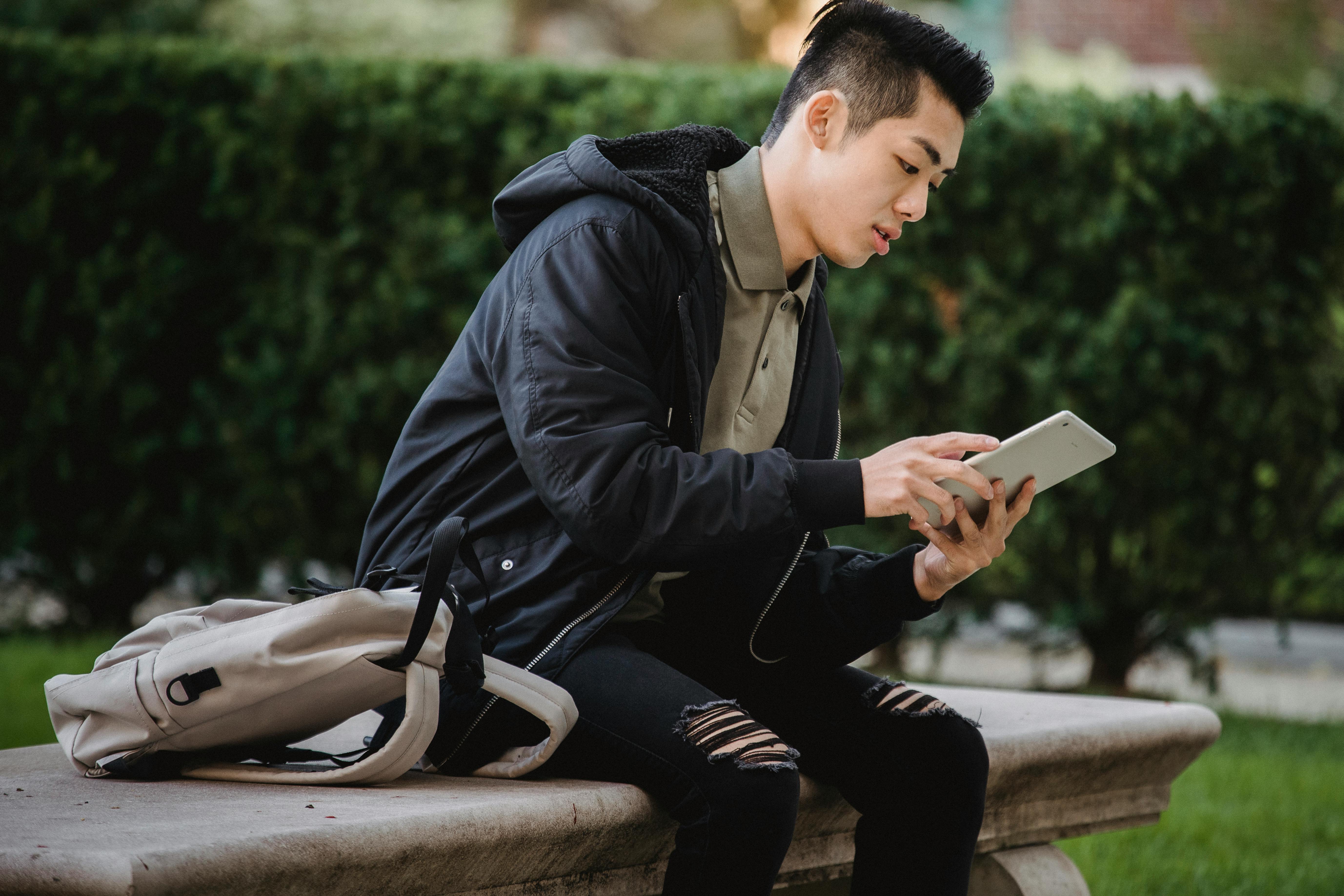 serious ethnic student using tablet on bench