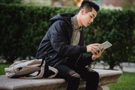 年轻人坐在公园长凳上，专注地使用着平板电脑