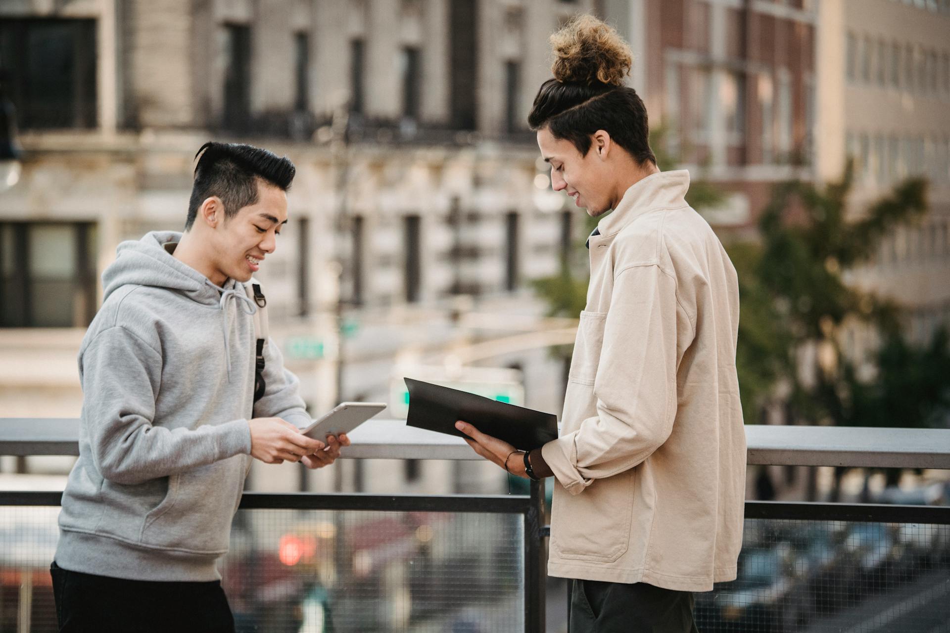 Side view of cheerful young multiracial male friends in casual outfits with tablet and folder with papers discussing new project on street