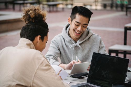 Free Positive young multiethnic male students in casual clothes sitting at table and laughing while working together on project Stock Photo