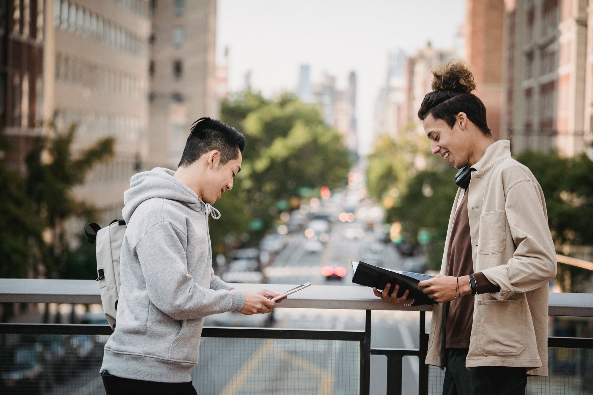 Side view of positive young multiracial male colleagues in casual clothes with tablet and papers in folder talking about new project