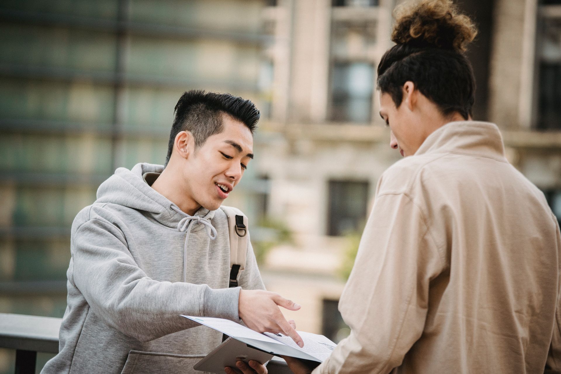 Side view of young multiracial male students in casual wear talking about papers on new project in folder
