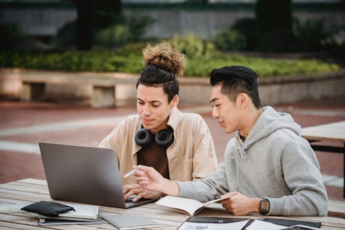 Free Serious young diverse male students in casual wear sitting at table with laptop and documents while working together on homework Stock Photo
