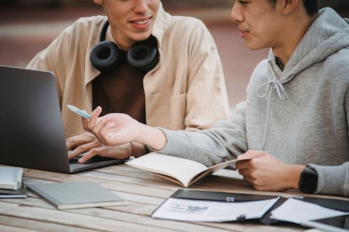Free Crop anonymous multiethnic male students in casual clothes at table with notebook and laptop working on assignment together Stock Photo