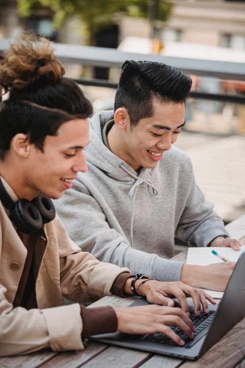 Free Happy young multiracial male students in casual clothes sitting at table while working on homework together Stock Photo