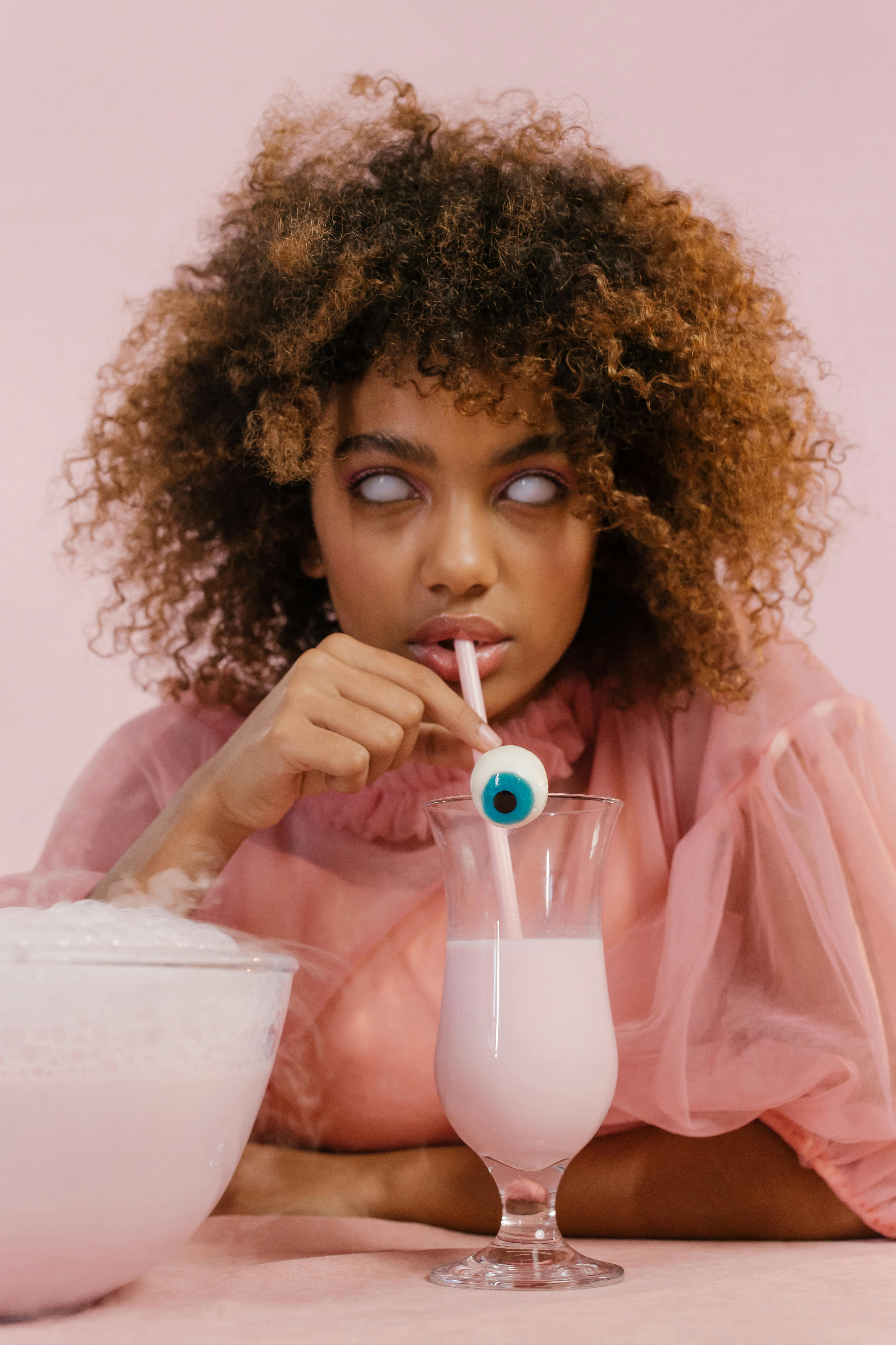 这是一幅以青少年为主题的超现实女子肖像，粉红色饮料里插着一根独特的眼球吸管