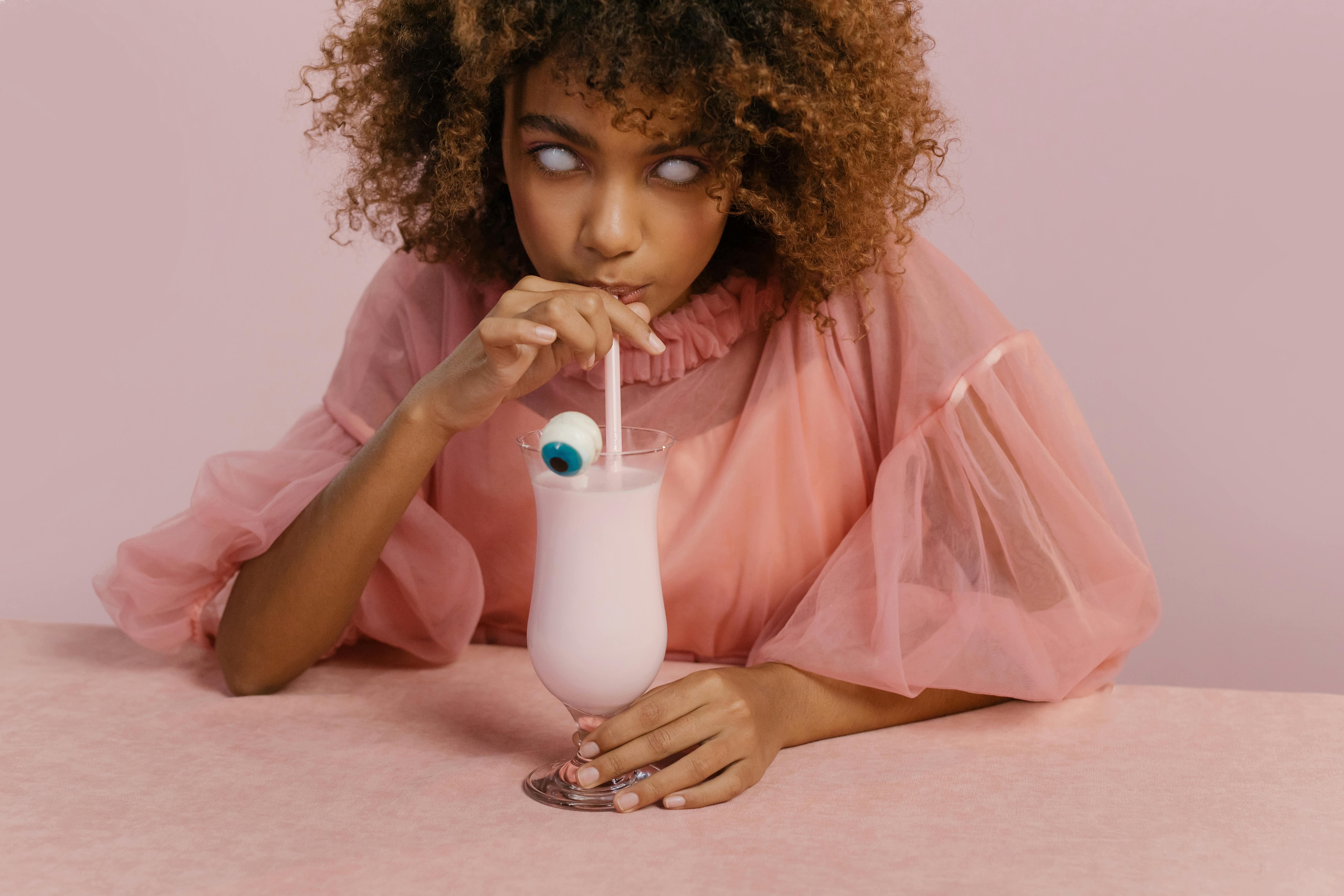 一位穿着创意万圣节服装的年轻女子正在喝一杯装有糖果眼球的奶昔