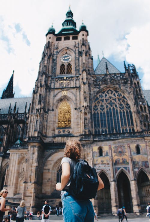 Free Woman Wearing Backpack And Grey Shirt Near Brown Church Stock Photo