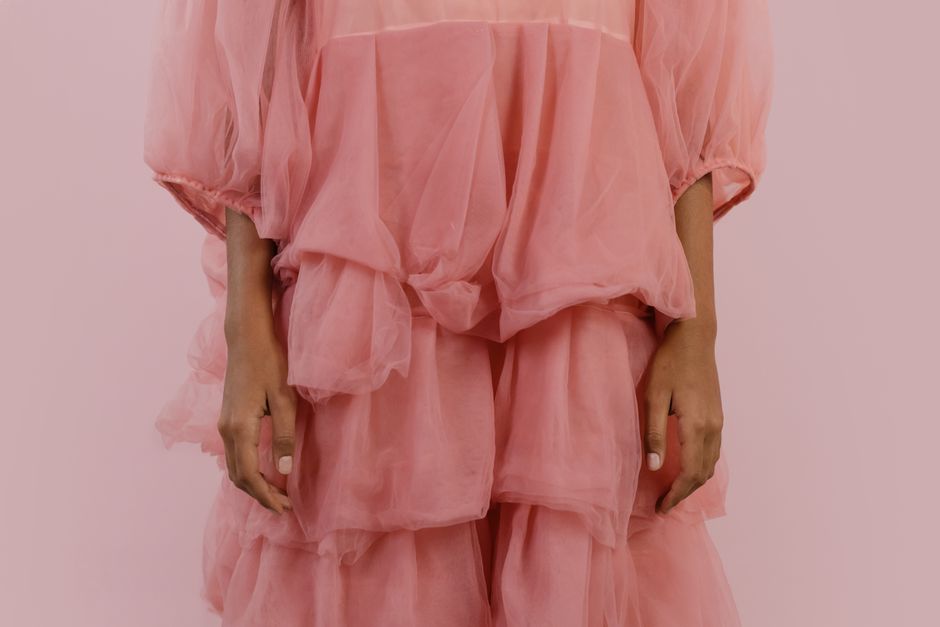 A close-up fashion shot of a person in an elegant pink gauze dress against a matching background.
