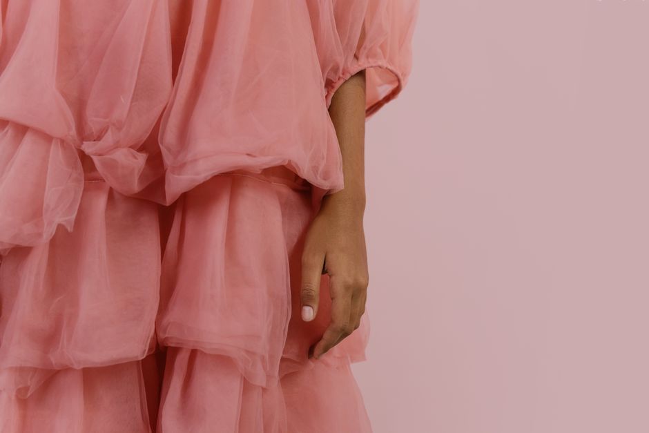 Close-up of a hand resting against a pink tulle dress with layered designs, set against a soft pink background.