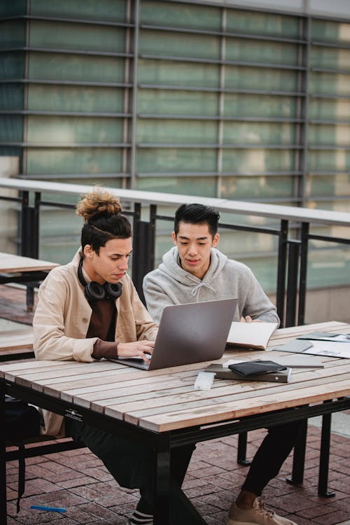 Focused young multiracial male students in casual wear looking at screen of laptop at table while working on project together