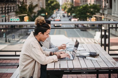 Free Side view of smiling young diverse male students in casual wear sitting at table with laptop and surfing internet while working on project together Stock Photo