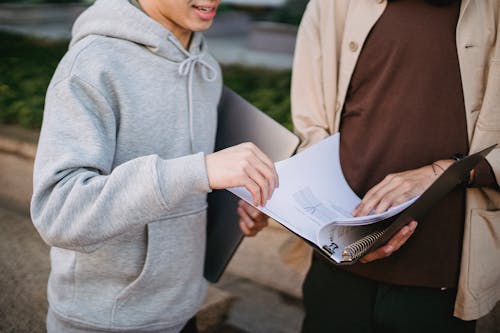 Crop male students reading article in folder in park