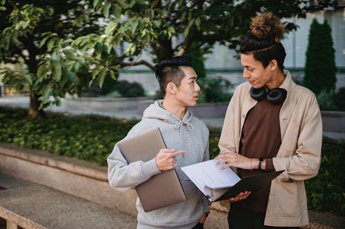 Positive diverse male students with textbooks discussing homework in park