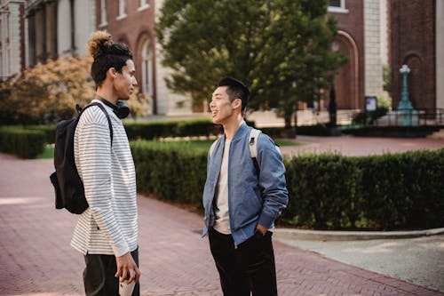 Content young multiethnic male friends wearing casual clothes standing on sidewalk and having conversation