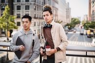 白天，两个年轻人拿着笔记本电脑和咖啡，站在充满活力的城市街道上