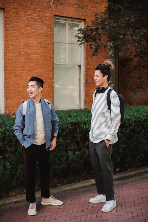 Full body of diverse students with backpacks and hands in pockets standing in park and  smiling together