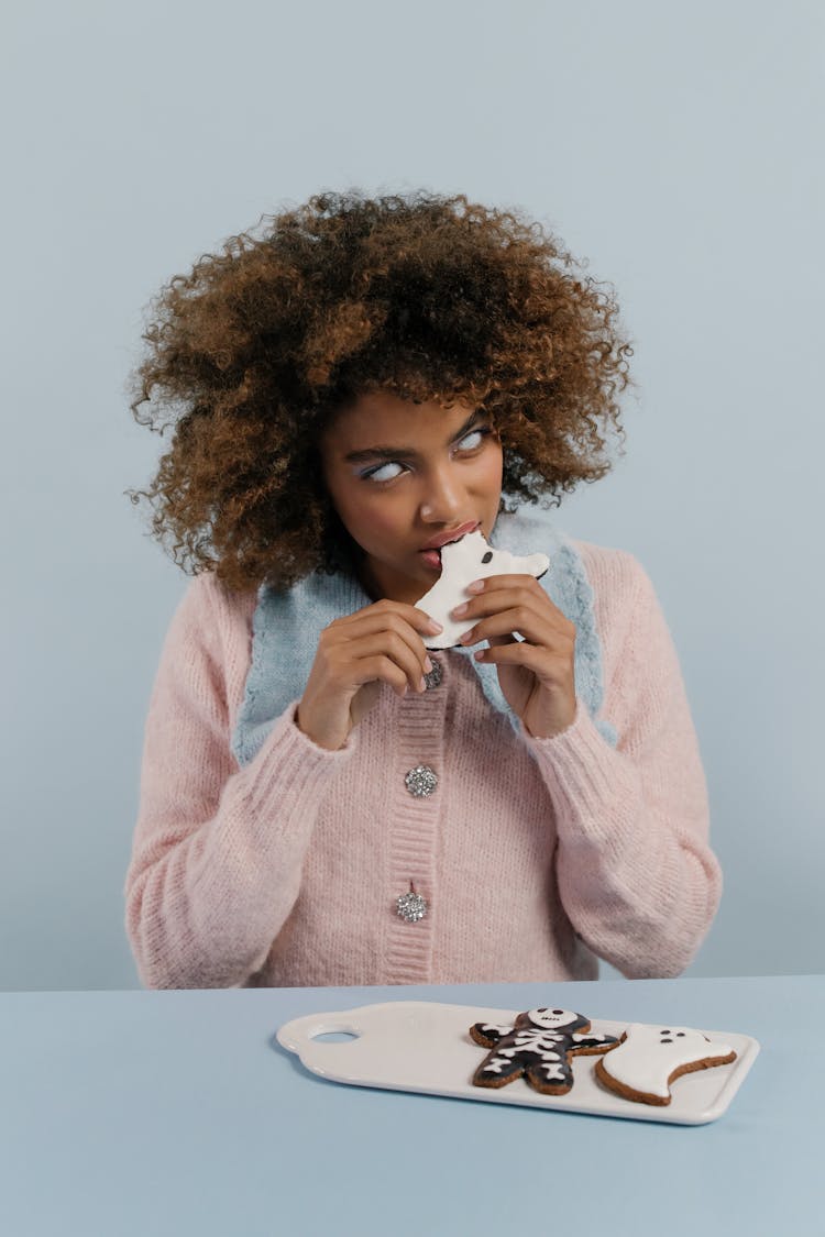 Woman In Pink Sweater Eating A Halloween Cookie