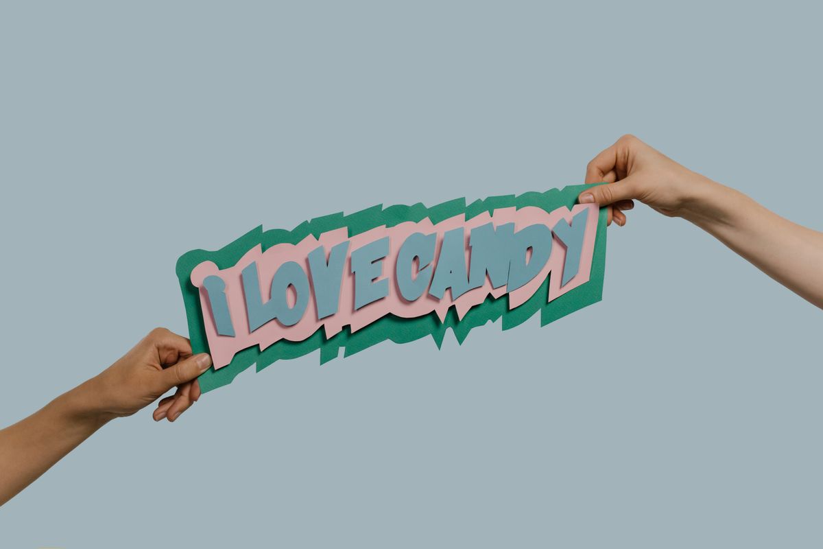 Two hands holding a colorful 'I Love Candy' paper cutout against a blue background.