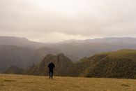 阴天，一名面目全非的男子走在山峰环绕的草地上，留下背影